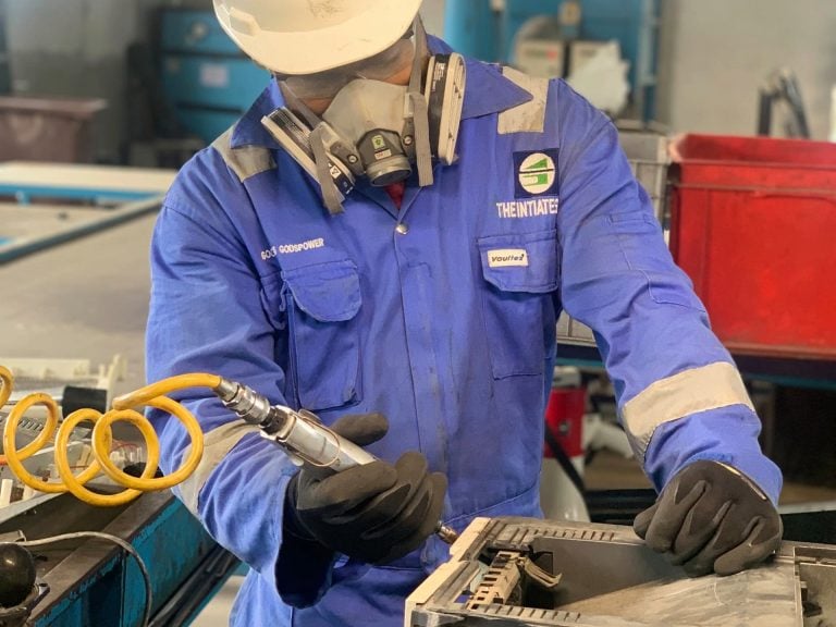 Man in protective gear dismantling electronic equipment, illustrate story on the 2 share offers by The Initiates PLC on Nigerian Exchange