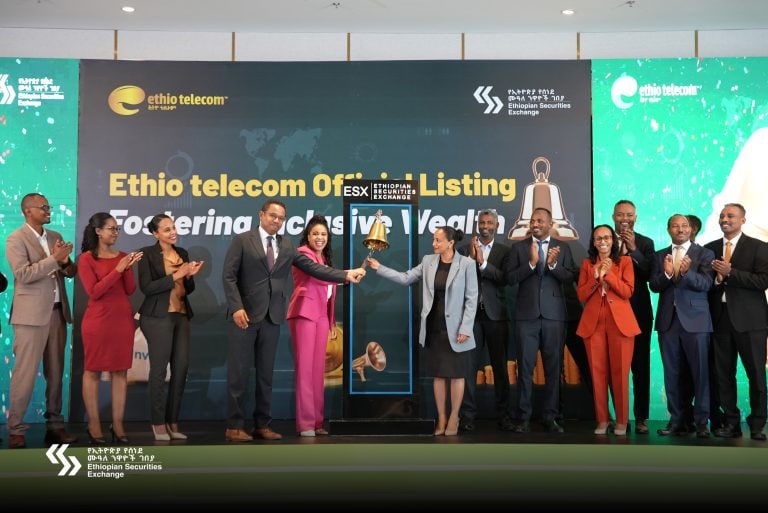 A large group of Ethiopian men and women in formal attire on a stage with a bell, celebrating Ethio Telecom, the fourth listing on the Ethiopian Securities Exchange.