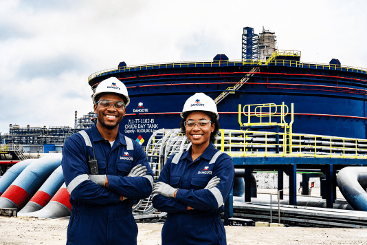main and woman smiling in overalls and hard hats in front of Dangote refinery oil tank