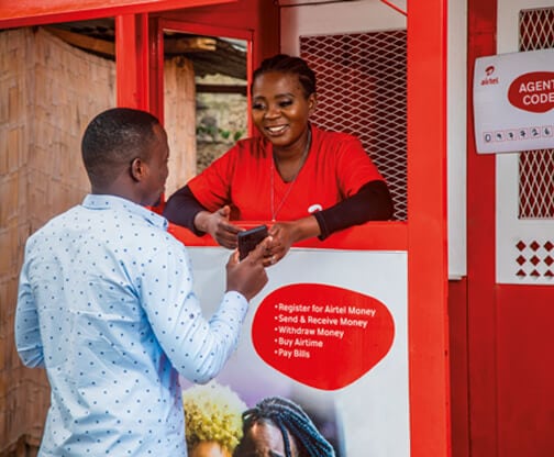 Man chatting to woman in Airtel mobile money booth ahead of Airtel Money IPO on London Stock Exchange.